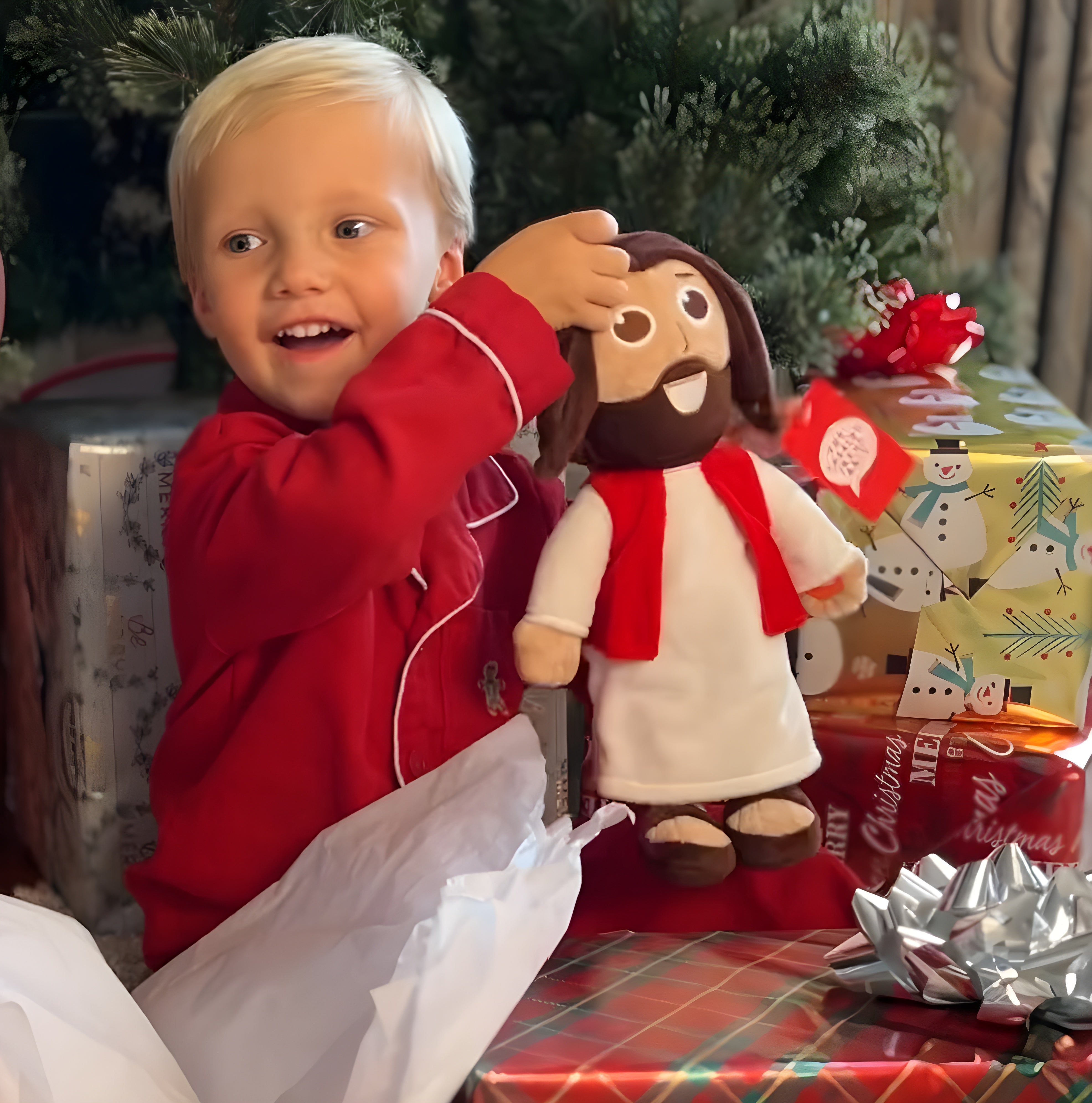 A young child in a red pajama top holds  The Talking Jesus Doll from jesusdoll.com. 